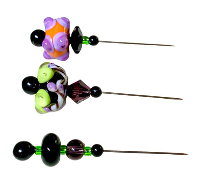 Three handmade lampwork bead pins with colorful patterned beads and black faceted beads, arranged vertically on a white surface.
[additional_image_link]