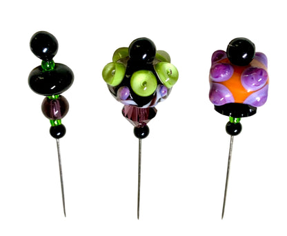 Three handmade glass bead pins with long metal spikes, displayed on a white background. The left pin has black and purple beads with green accents.
[additional_image_link]