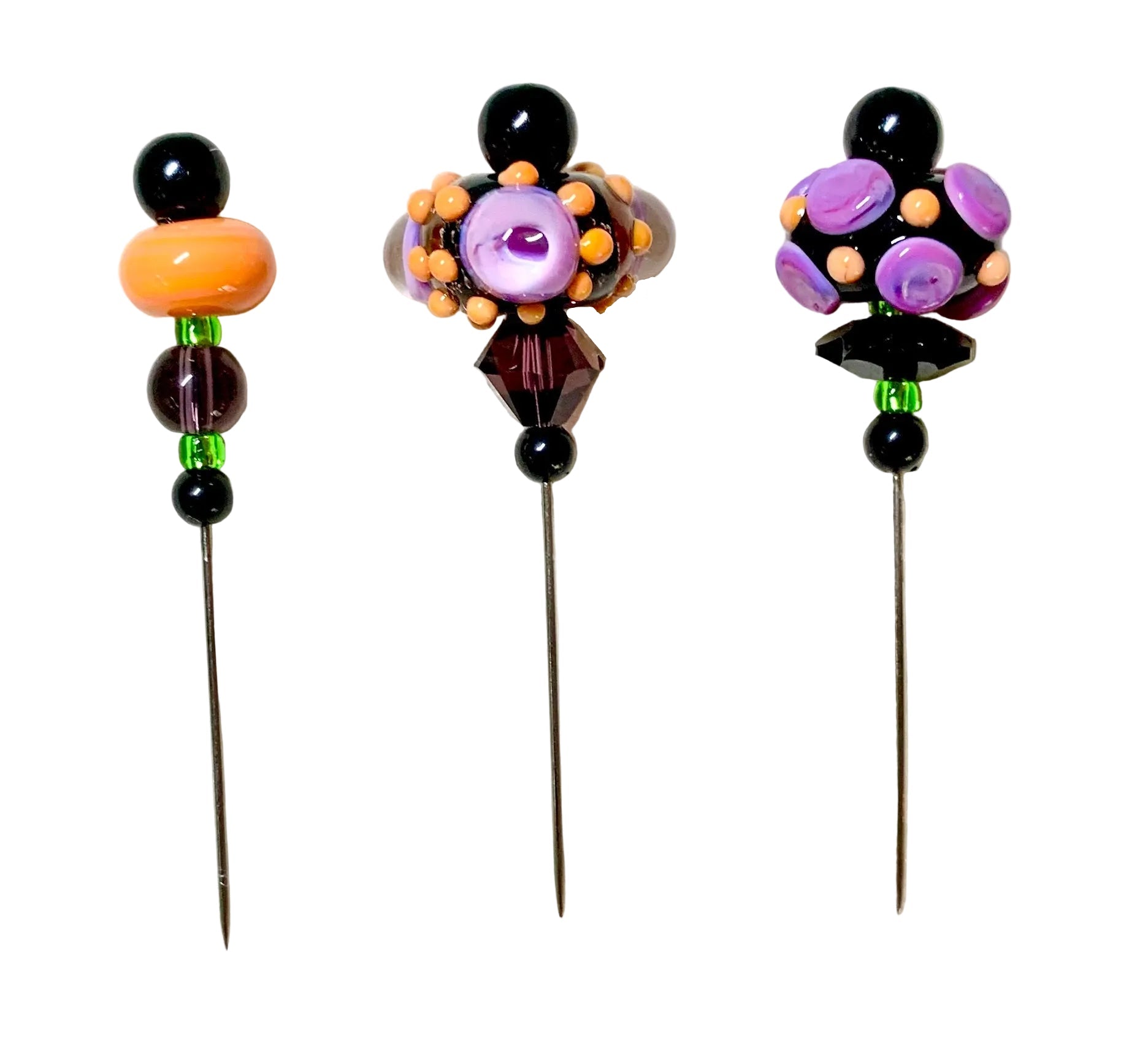 Three decorative beaded pins with long metal needles, displayed on a white background. The left pin features black beads, a large orange bead, and green and purple beads.
[image_link]