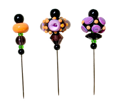 Three decorative beaded pins with long metal needles, displayed on a white background. The left pin features black beads, a large orange bead, and green and purple beads.
[image_link]