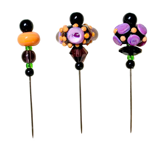 Three decorative beaded pins with long metal needles, displayed on a white background. The left pin features black beads, a large orange bead, and green and purple beads.
[image_link]