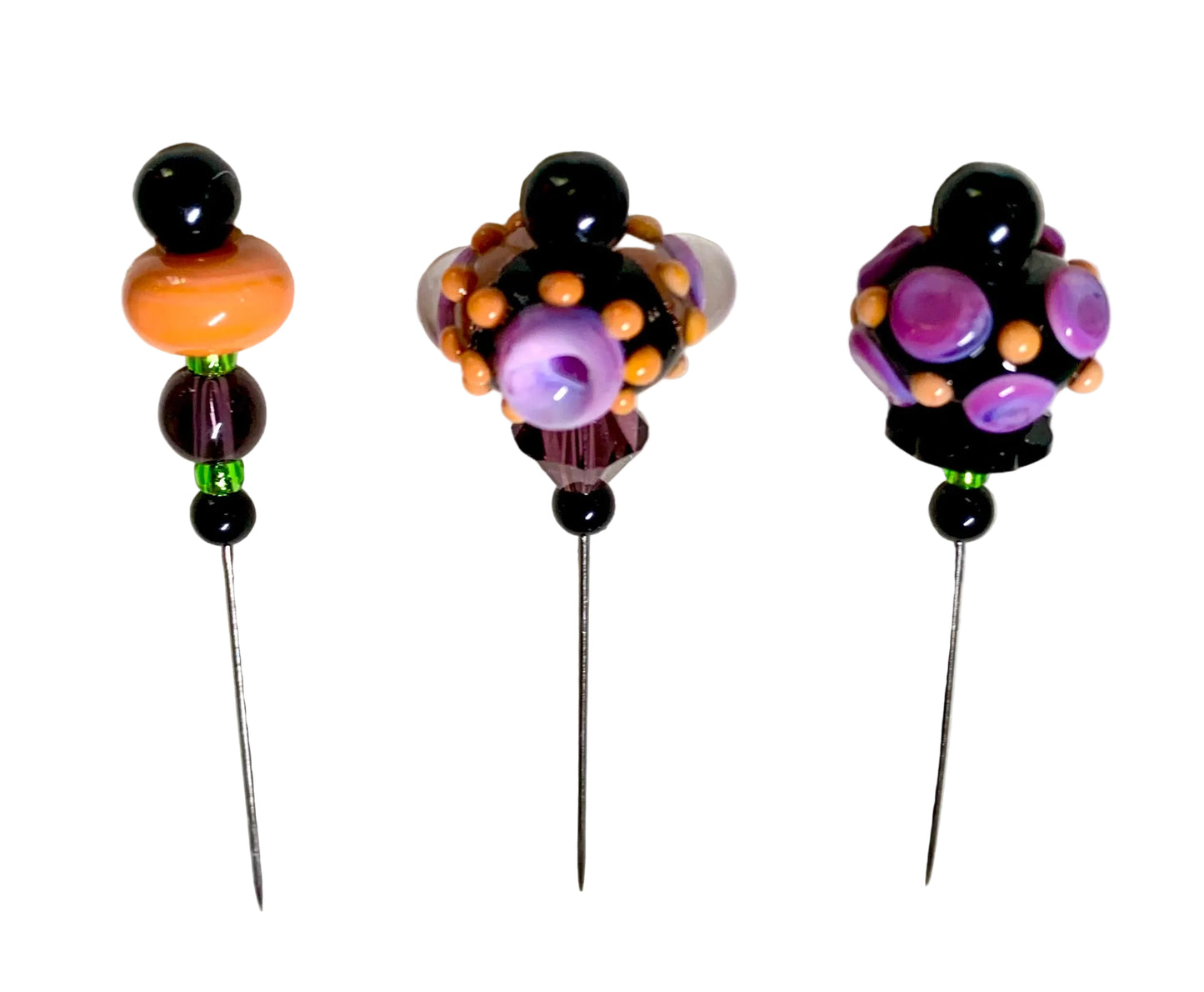 Three decorative beaded pins with long metal spikes are arranged on a light textured background. Each pin has black beads, orange and purple glass beads, and small green accent beads.
[additional_image_link]