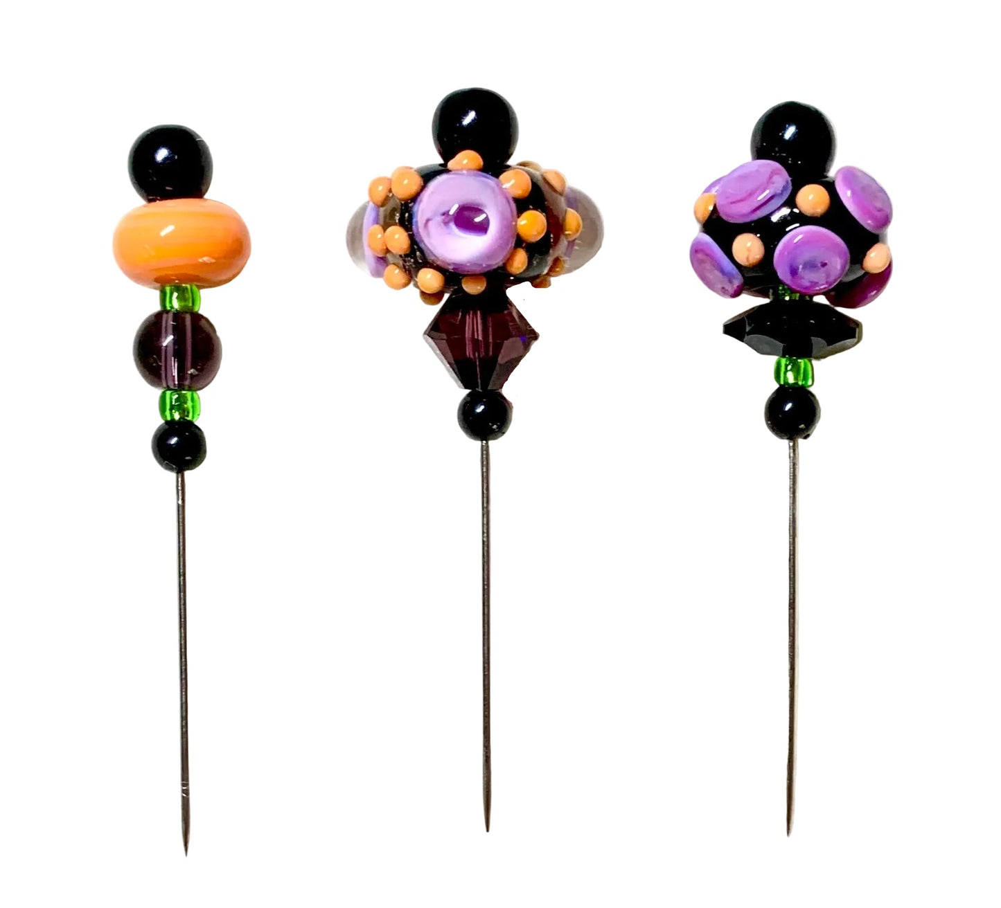 Three decorative beaded pins with long metal needles, displayed on a white background. The left pin features an orange bead and green accents, the middle pin has a purple flower design with orange beads, and the right pin showcases purple and orange flower-like beads.
[additional_image_link]
