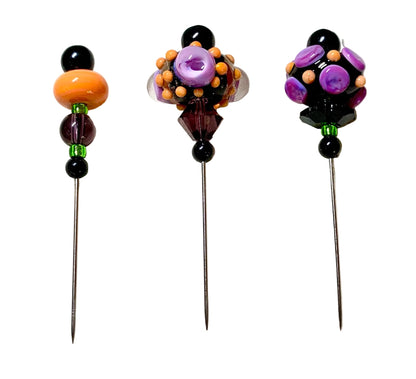 Three decorative glass pinback needles with colorful beaded tops on a white fabric background.
[additional_image_link]