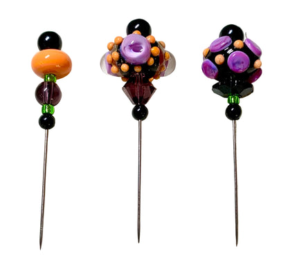 Three decorative glass lampwork pins with long metal needles, displayed on a white background. The pins feature colorful glass beads including purple, orange, black, and green.
[additional_image_link]