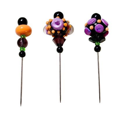 Three handmade bead pins with long metal pins are displayed on a white background. Each pin features a unique design of colorful beads, including purple, orange, black, and green, with one pin featuring a prominent orange bead and the others featuring purple and black beads.
[additional_image_link]