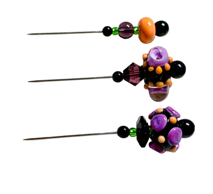 Three beaded sewing pins with purple, black, orange, and green beads arranged vertically on a white surface.
[additional_image_link]