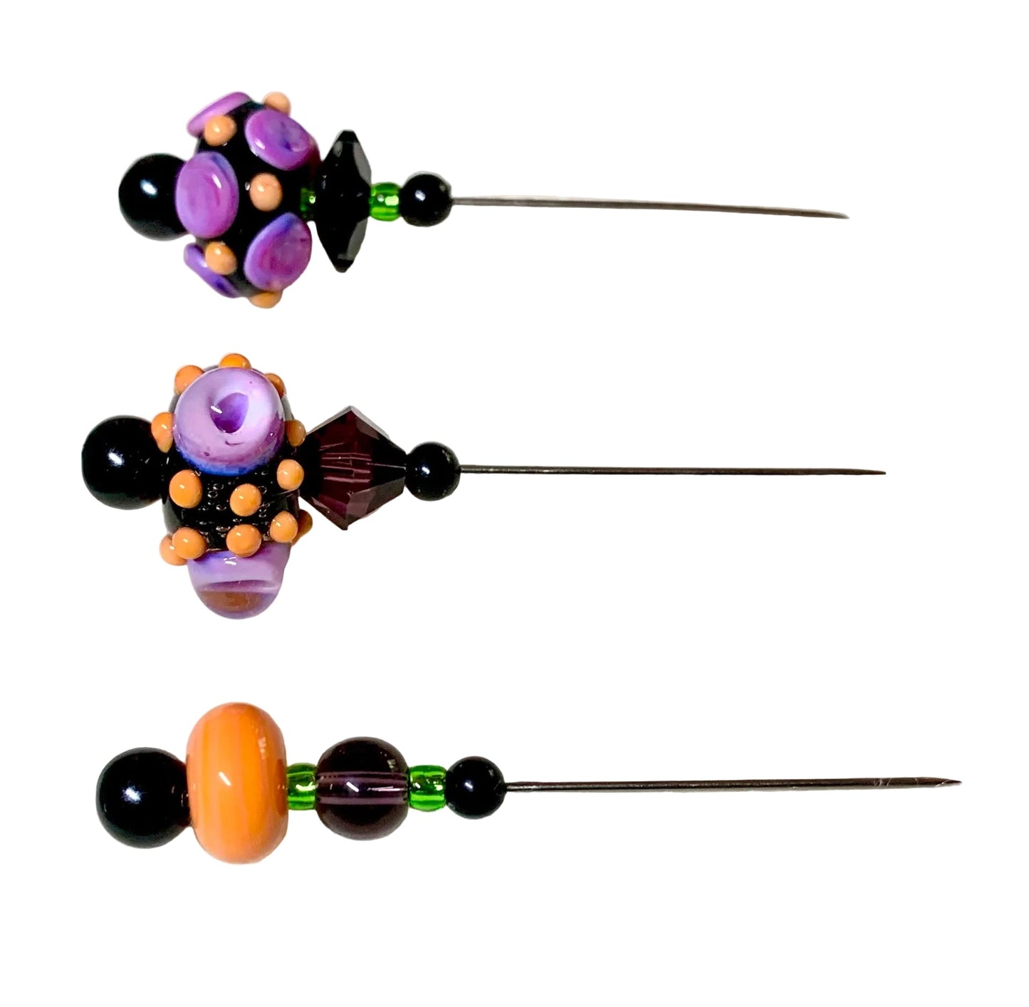 Three handmade beaded pins with long metal needles, decorated with colorful glass beads in purple, orange, black, and green, displayed on a white background.
[additional_image_link]