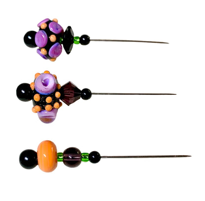 Three handmade beaded pins with long metal needles, decorated with colorful glass beads in purple, orange, black, and green, displayed on a white background.
[additional_image_link]