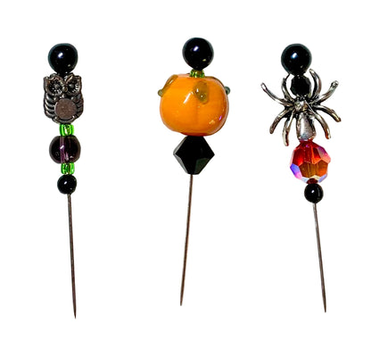 Three Halloween-themed beaded pins on a white background. The left pin features a silver owl and green beads. The right pin features a silver spider with a fiery red orange faceted bead. The middle pin has a lampwork pumpkin with black bead.
[additional_image_link]