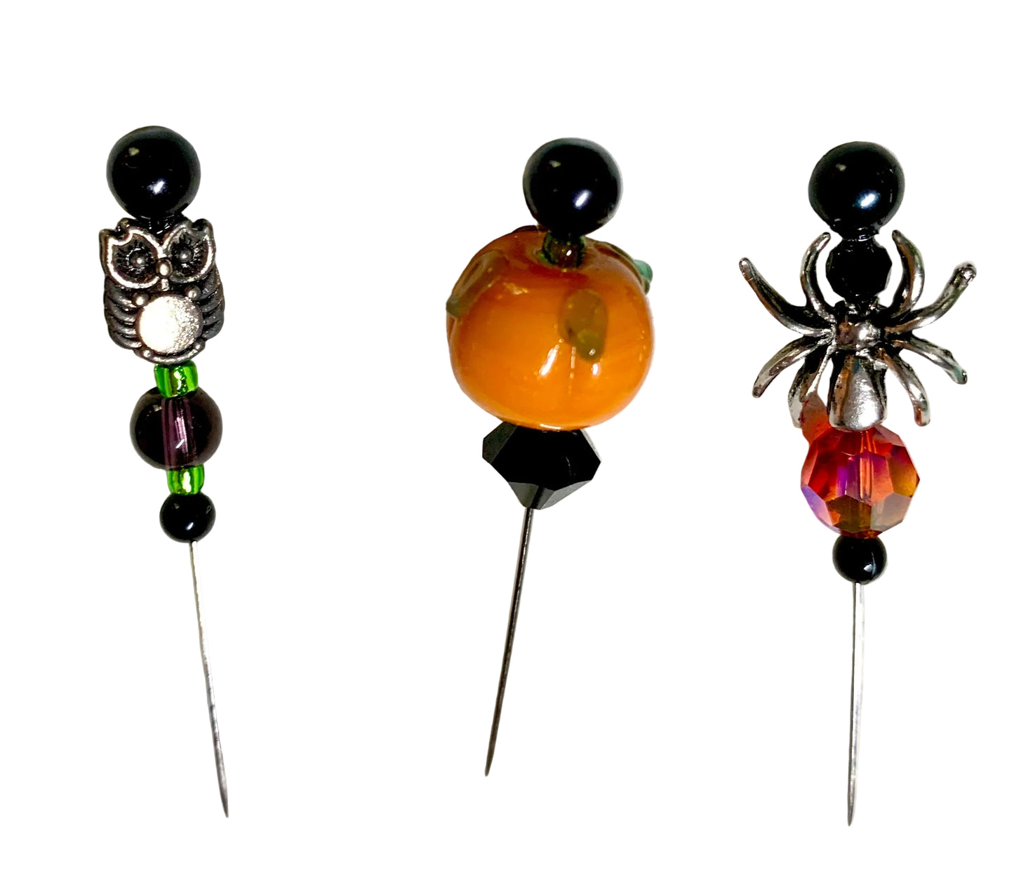Three Halloween-themed beaded pins on a white background. The left pin features a silver owl with purple and black beads. The right pin has a silver spider with a fire bead. The middle is a lampwork pumpkin with black bicone bead.
[additional_image_link]