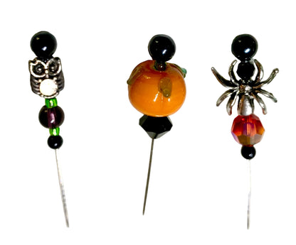 Three Halloween-themed beaded pins on a white background. The left pin features a silver owl, green beads, and black beads. The right pin has a silver spider with a fire bead. The middle is a lampwork pumpkin with black bicone.
[additional_image_link]