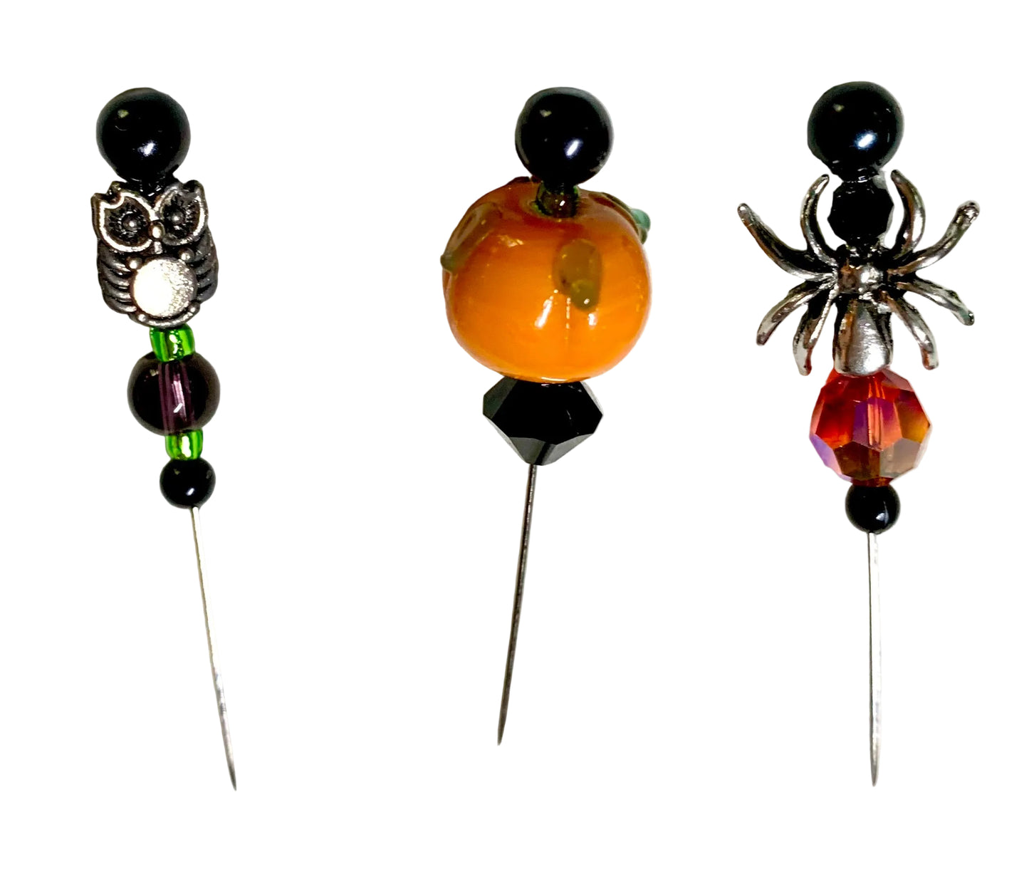 Three Halloween-themed beaded pins on a white background: an owl pin with silver and black beads, a pumpkin pin with an orange bead and black faceted bicone, and a spider pin with a silver spider and red faceted bead.
[additional_image_link]
