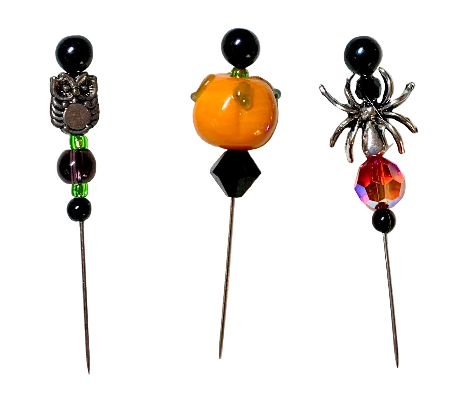 Three Halloween-themed beaded pins on metal needles, featuring an owl, a pumpkin, and a spider design with black beads, a small green bead, a faceted black diamond, and an iridescent red crystal.
[additional_image_link]
