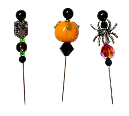 Three Halloween-themed beaded pins on metal needles, featuring an owl, a pumpkin, and a spider design with black beads, a small green bead, a faceted black diamond, and an iridescent red crystal.
[additional_image_link]
