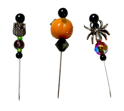 Three Halloween-themed beaded pins on metal needles, featuring an owl, a pumpkin, and a spider design, displayed on a white background.
[additional_image_link]