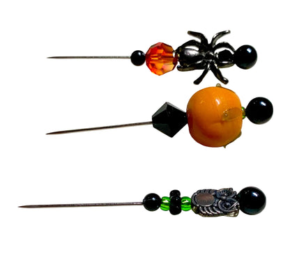 Three decorative sewing or embroidery pins with Halloween-themed bead and metal embellishments, displayed on a white surface. There is a silver owl charm, a black spider charm and a lampwork pumpkin.
[additional_image_link]