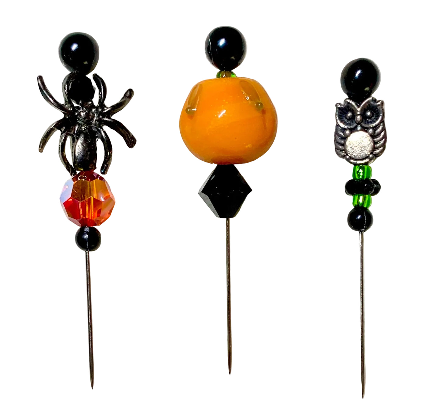 Three Halloween-themed beaded pins on a white background. The left pin features a silver spider and a faceted orange-red bead. The right pin has a silver owl charm and the middle has a lampwork pumpkin.
[image_link]