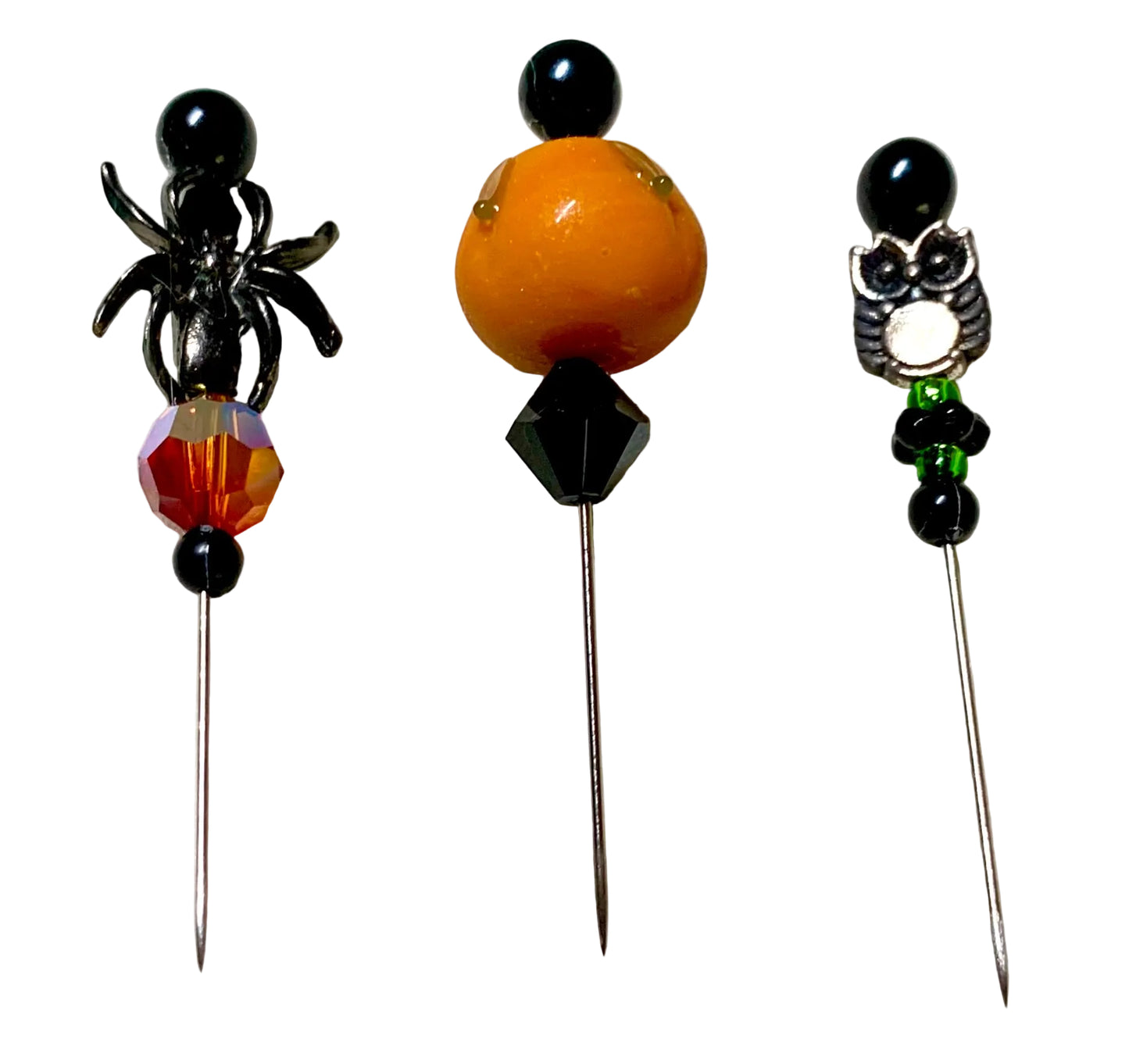 Three Halloween-themed beaded pins on a white background. The left pin features a black spider and a faceted amber-red bead. The right pin has a silver owl and the middle has a lampwork pumpkin.
[additional_image_link]