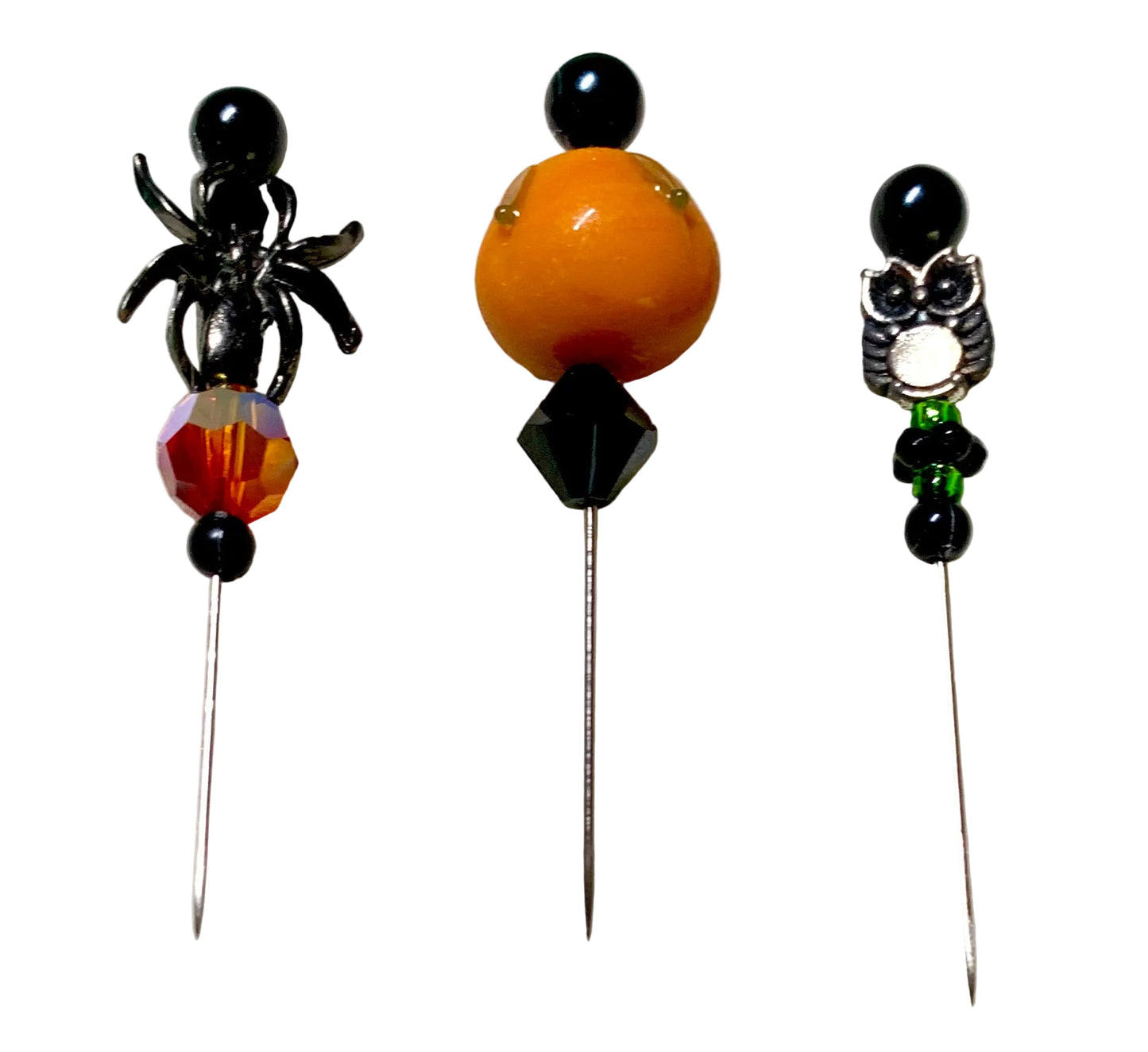 Three Halloween-themed beaded pins displayed on a white background. The left pin features a black spider, a faceted orange and black bead, and a crystal bead. The middle bead is a lampwork pumpkin with black bicone bead and the right has a silver owl with black and green beads.
[additional_image_link]