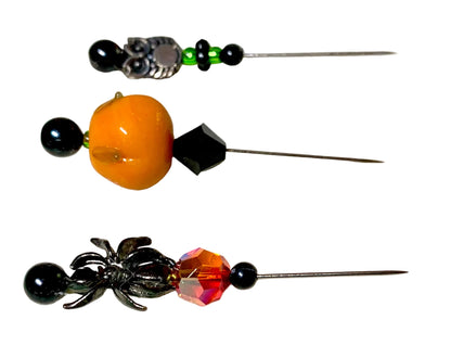 Three Halloween-themed beaded pins with black beads, a glossy orange pumpkin, a black faceted bicone, a silver spider, and a faceted fire crystal on a white background. There is a silver owl with green and black beads.
[additional_image_link]