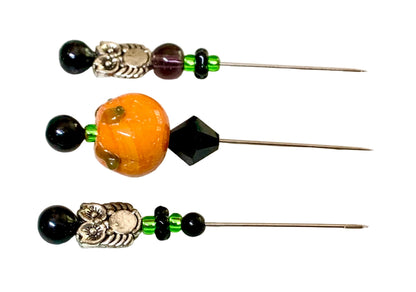 Three decorative sewing pins with beads and metal owl charms  and a pumpkin bead laid horizontally on a white background.
[additional_image_link]