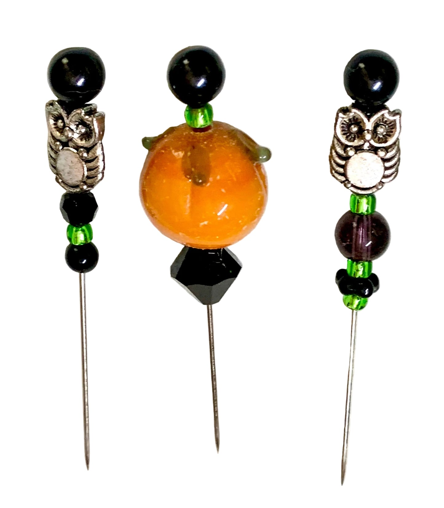 Three beaded pins with owl charms and silver needles, displayed on a white surface. The left and right buttons feature black beads, green accents, and silver owl details, while the center button features a prominent orange pumpkin bead.
[additional_image_link]