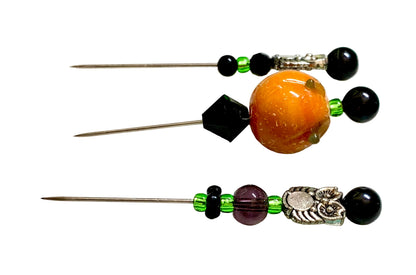 Three beaded sewing pins with black beads, green accent beads, a large orange pumpkin bead, a purple faceted bead, and silver-toned metal owl accents, displayed on a white background.
[additional_image_link]