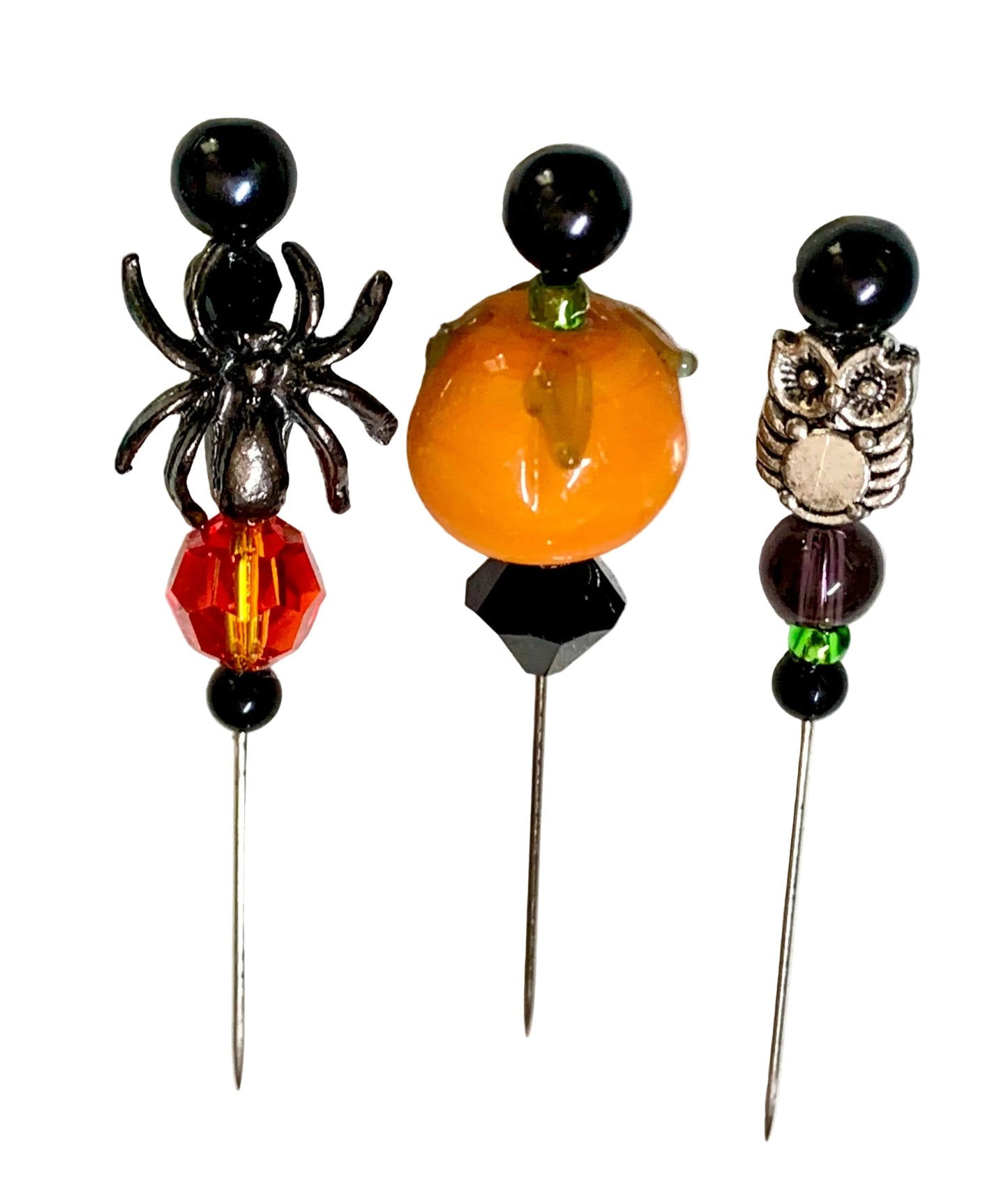 Three Halloween-themed beaded pins on a textured white background. The left pin features a black spider and a red faceted bead. The middle and right pins have a pumpkin and an owl.
[additional_image_link]