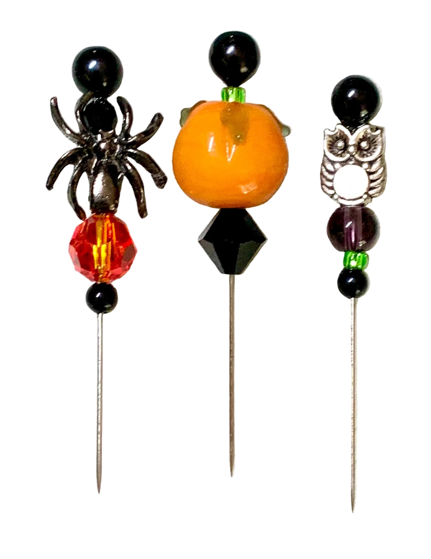 Three Halloween-themed beaded pins on a white background. The left pin features a black spider, a red faceted crystal bead, and black beads. The right pin is a silver owl. The middle is a pumpkin.
[additional_image_link]