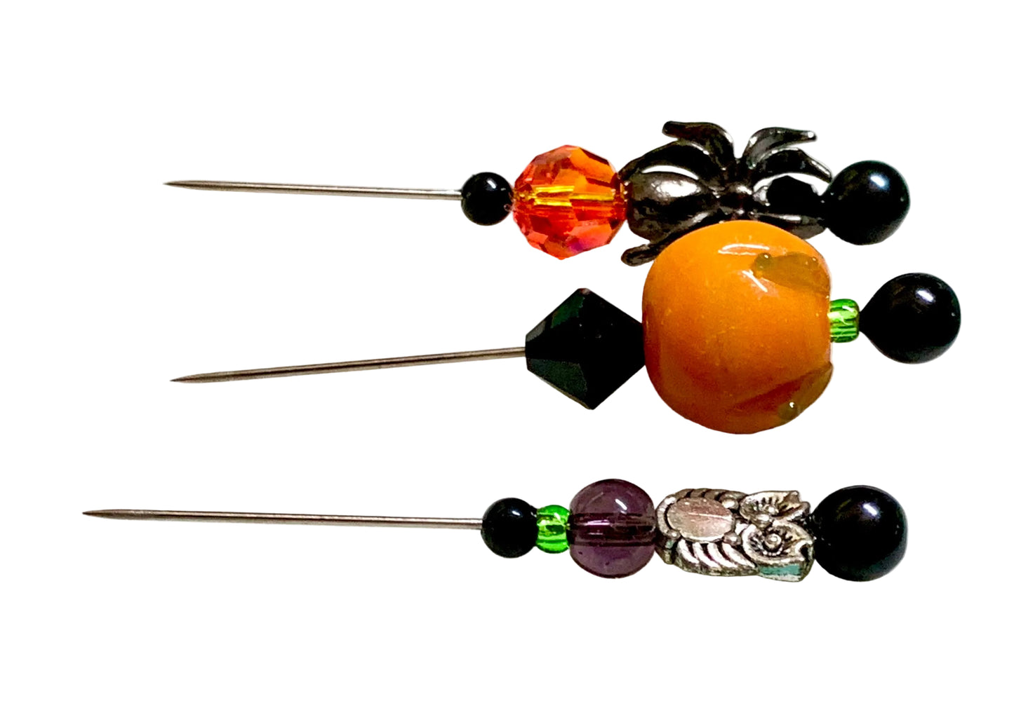 Three beaded sewing pins with orange, black, green, and silver beads, displayed on a white surface. The pins have a spider, an owl and a pumpkin.
[additional_image_link]