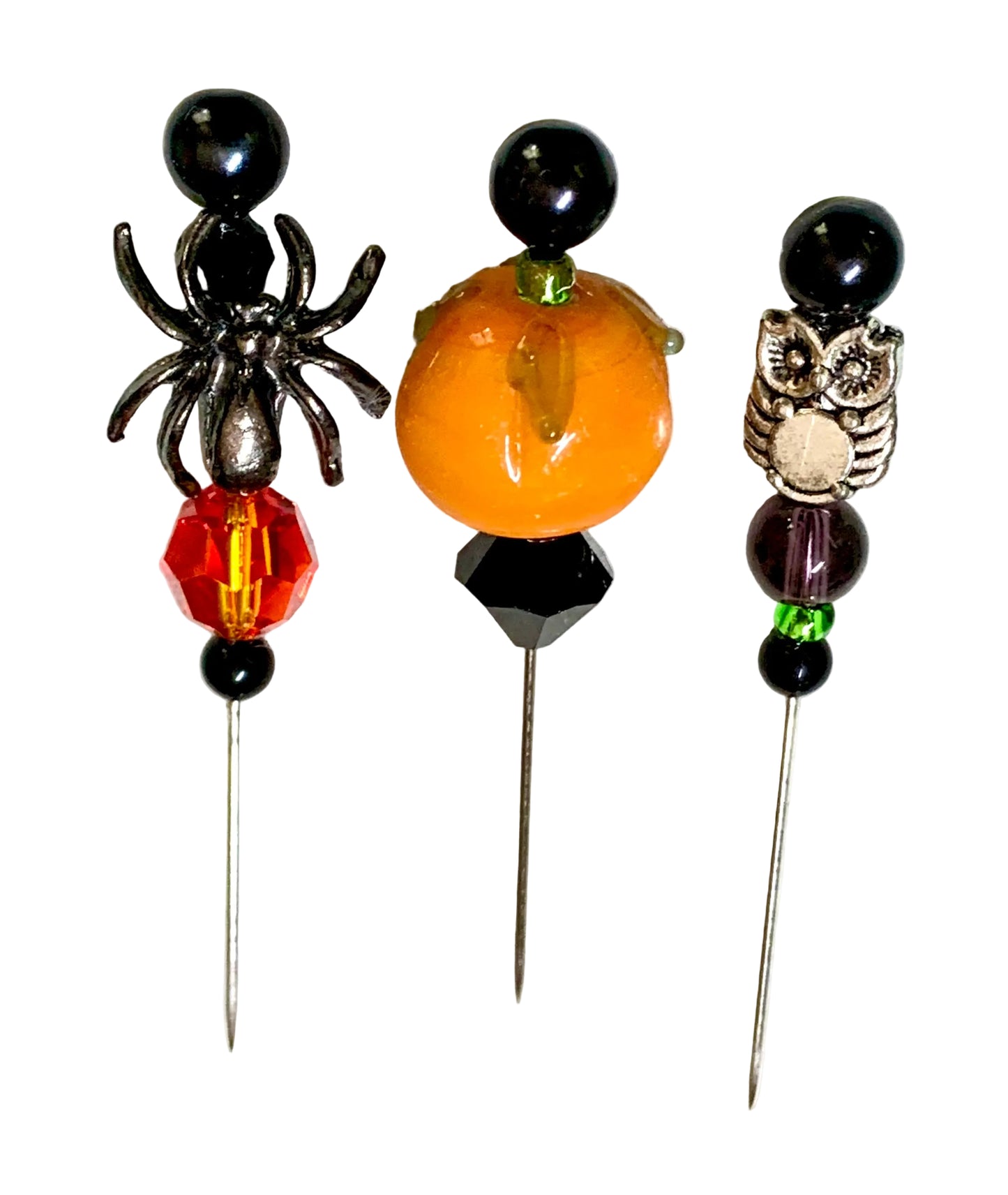 Three Halloween-themed beaded pins on metal needles, featuring a black spider, an orange pumpkin, and a silver owl, displayed on a white surface.
[additional_image_link]