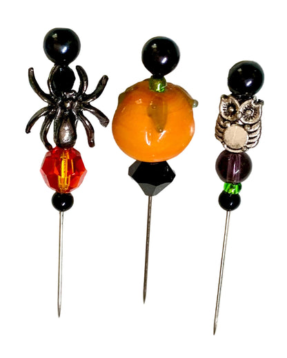 Three Halloween-themed decorative pins on a white background. The left pin features a black spider, a red faceted bead, and black beads. The middle and right pins have a pumpkin and owl charms.
[additional_image_link]