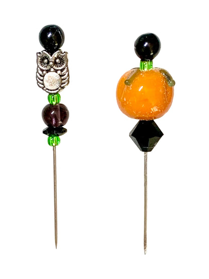 Two beaded pins, featuring a silver owl charm on the left and a glossy orange pumpkin bead with green and black accents on the right, set against a white background.
[additional_image_link]