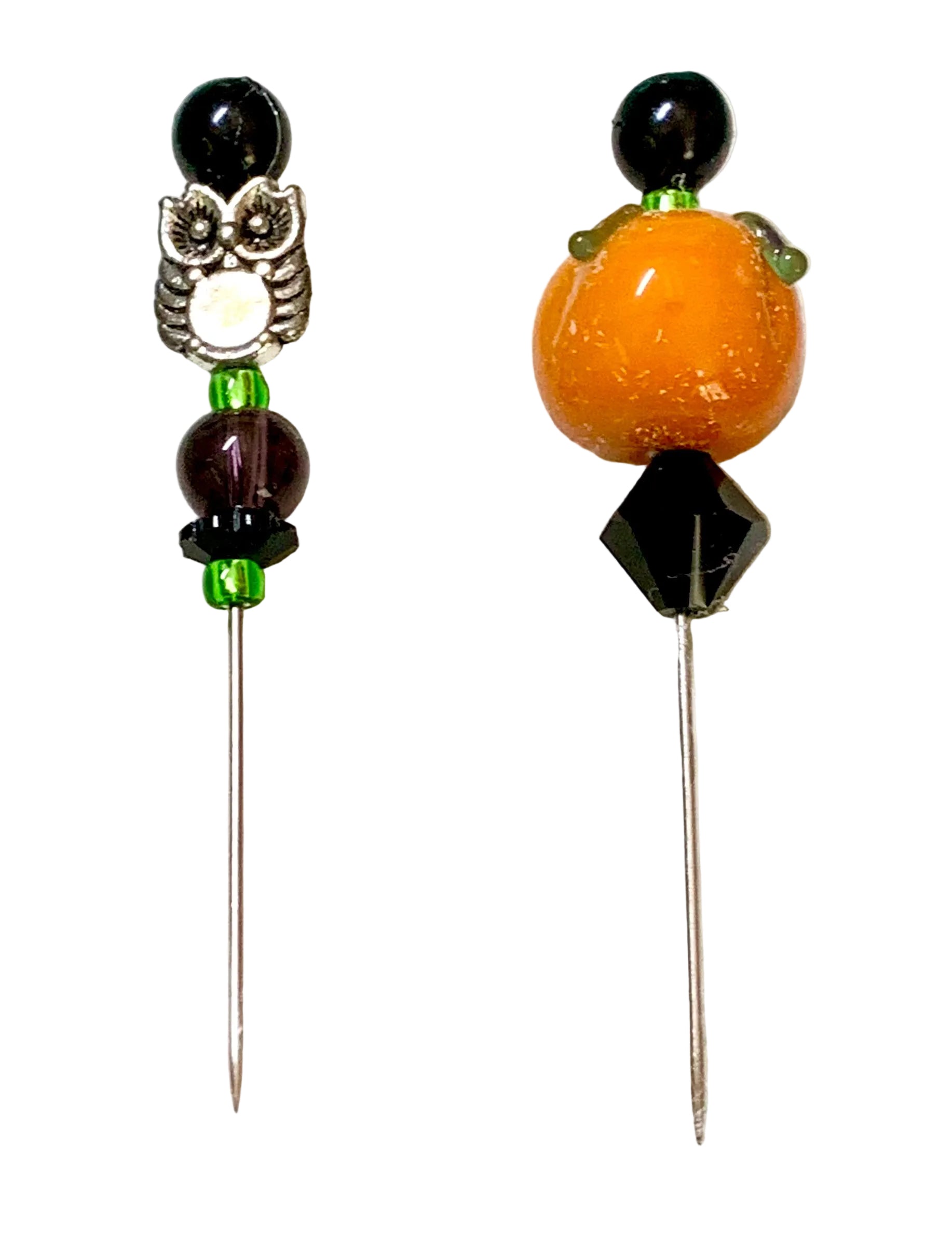 Two beaded pins on a white background. The left pin features a silver owl charm, dark brown beads, and green spacer beads. The other pin is a pumpkin.
[additional_image_link]