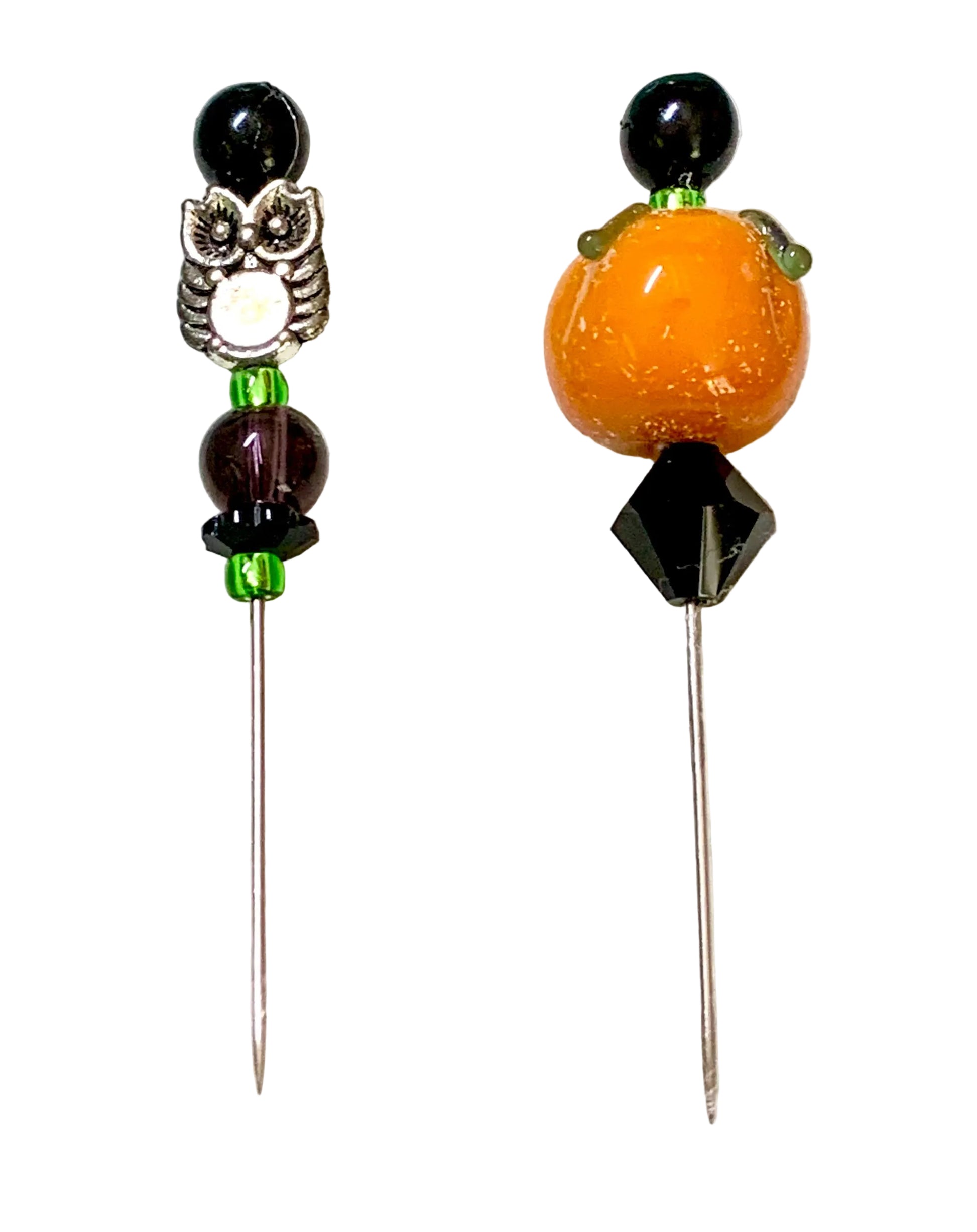 Two beaded pins displayed on a white surface. One pin features a silver owl charm with a white center, black beads, and green spacer beads. The other is a pumpkin.
[additional_image_link]