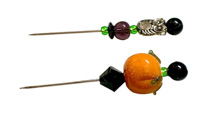 Two Halloween-themed pins with beads, shown on a white background. One pin features a purple bead, a silver owl, and a black bead. The other is a pumpkin.
[additional_image_link]