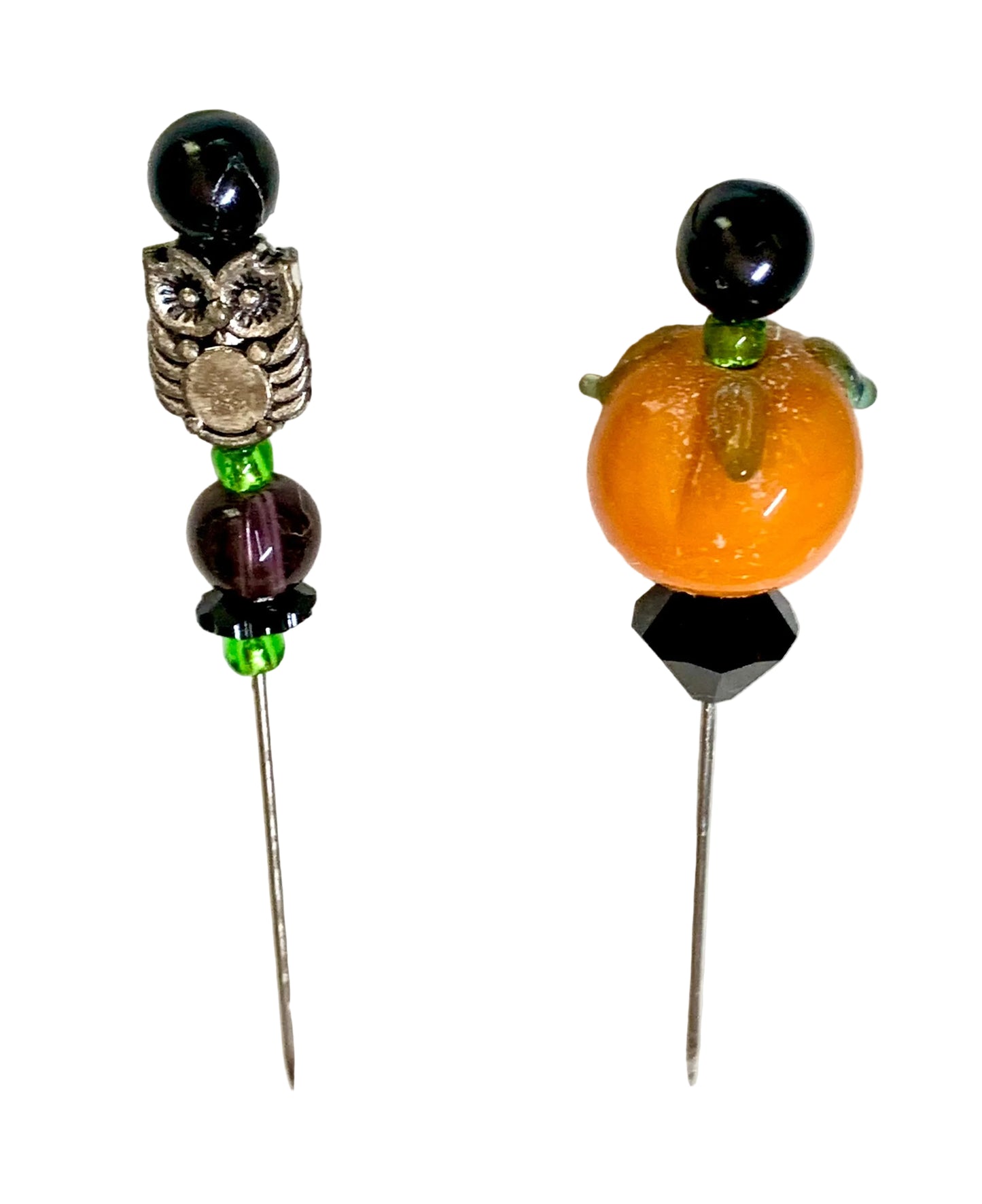 Two handmade beaded pins on a white background. One pin features a black bead, a silver owl charm, a dark purple bead, and green spacer beads. The other is a pumpkin.
[additional_image_link]