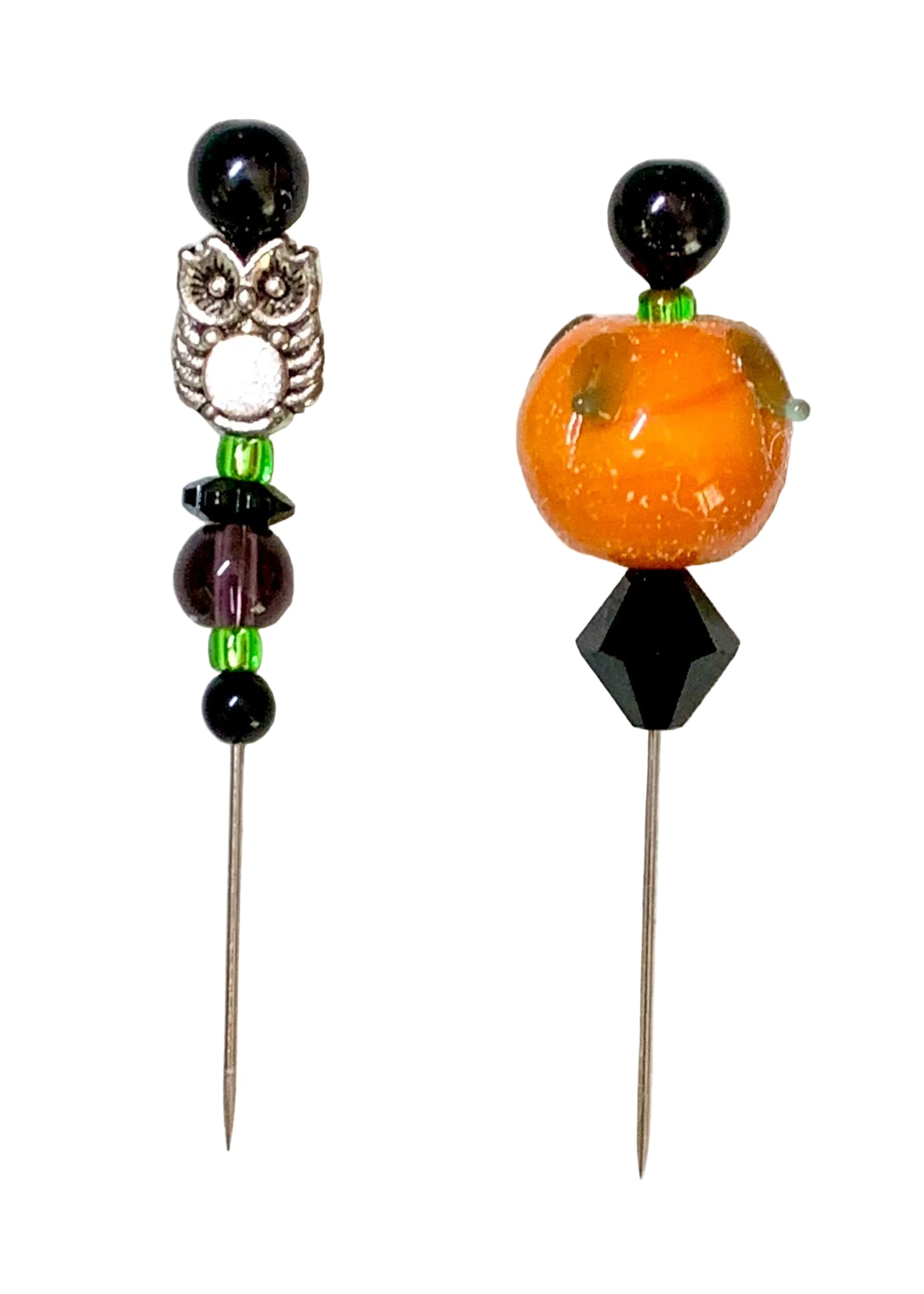 Two beaded pins displayed on a white background. The left pin features a silver owl charm, black beads, and green spacer beads. The other is a pumpkin.
[additional_image_link]