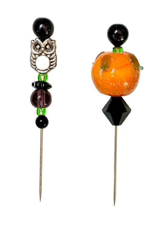 Two beaded pins, displayed on a white background. One pin features a silver owl charm with a white center, black beads, and green accents. The other is a pumpkin.
[image_link]