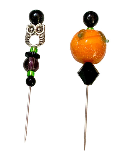 Two beaded sewing pins on a white background. One pin features a silver owl charm, black beads, and green spacer beads. The other pin is a pumpkin.
[additional_image_link]