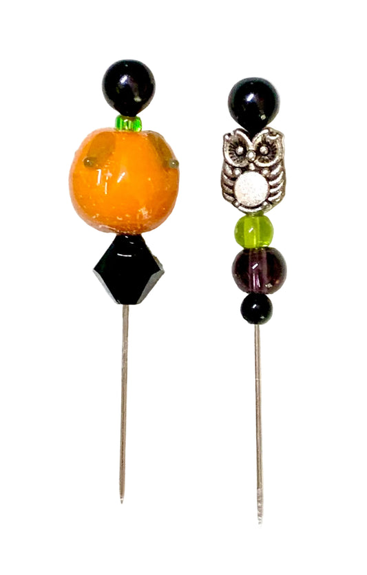 Two decorative beaded pins on a white background. One pin features a large orange  pumpkin bead, a black faceted bead, and a black round bead. The other is an owl bead.
[image_link]