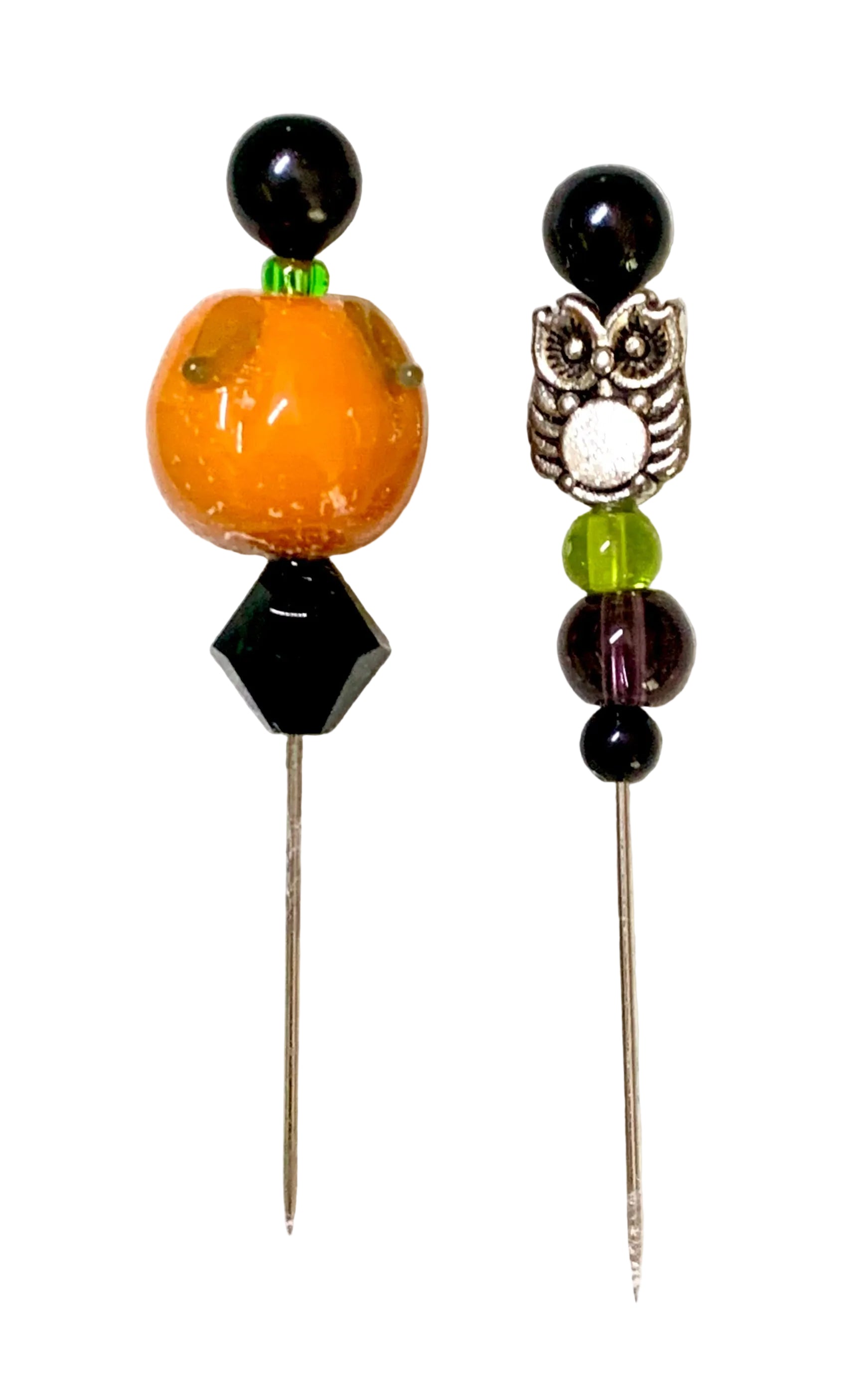Two beaded pins displayed on a white background. The left pin features a large orange pumpkin bead, a black faceted bead, and a black round bead at the top. The other is an owl.
[additional_image_link]