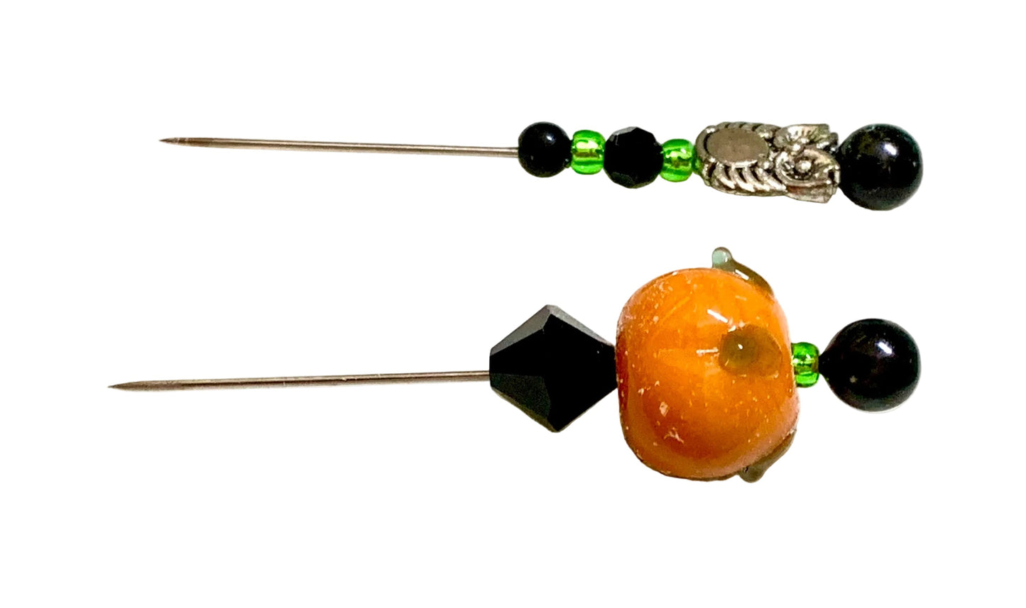 Two decorative sewing pins with black beads, green accent beads, a silver filigree charm, and a lampwork orange pumpkin bead on a white background.
[additional_image_link]