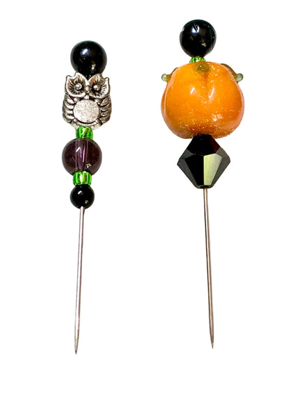 Two beaded pins, featuring black beads, a silver owl charm, a purple bead, and green accents on the left, and an orange pumpkin bead with a faceted black top on the right, set against a white background.
[additional_image_link]