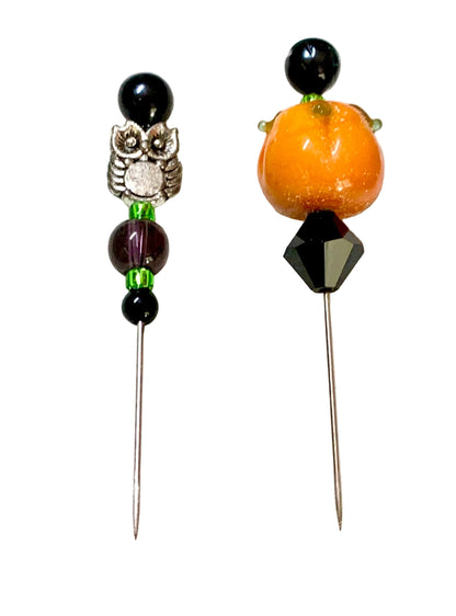 Two beaded pins displayed on a white surface. One pin features a silver owl charm, black beads, and green spacer beads. The other is a pumpkin bead.
[additional_image_link]
