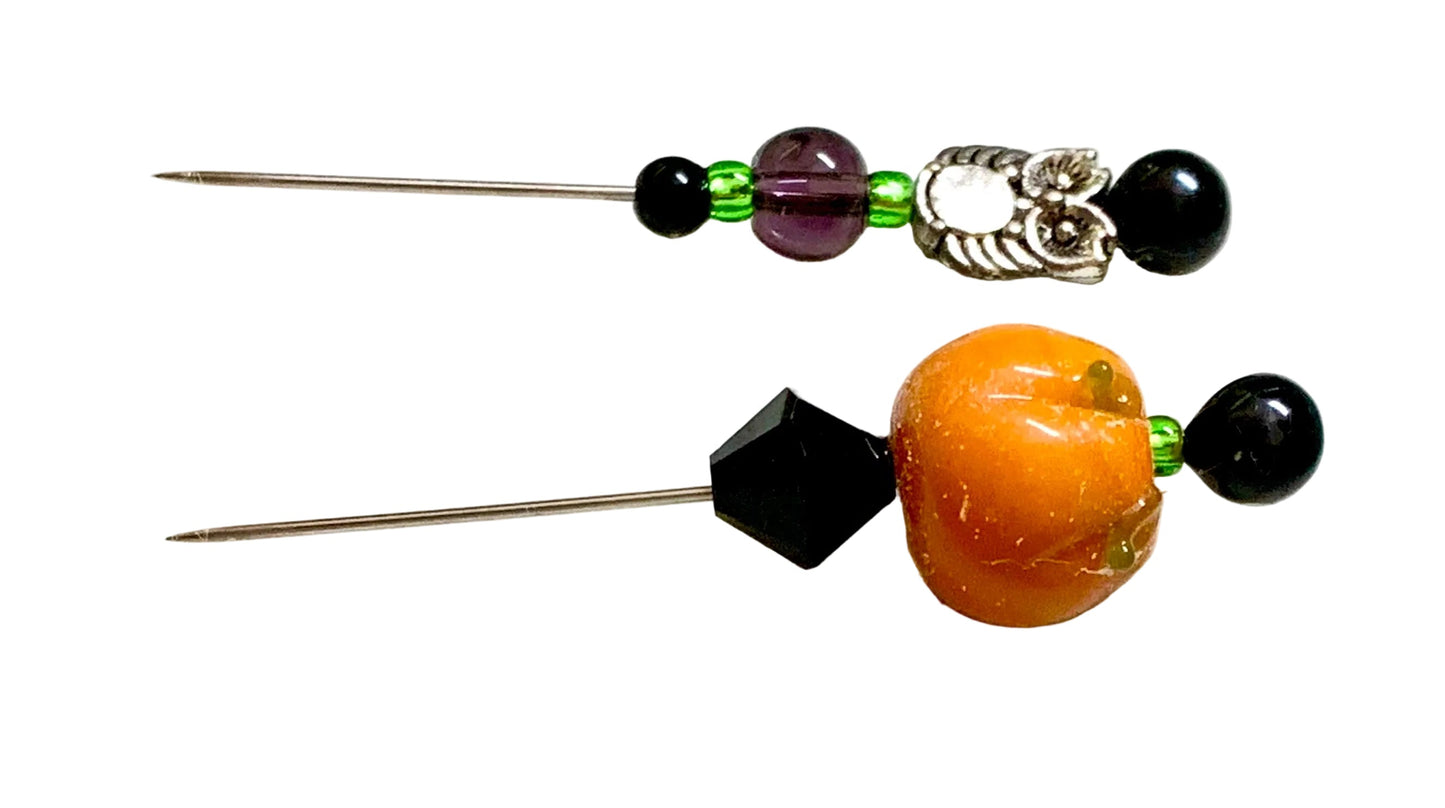 Two beaded pins displayed on a white background. One pin features a silver owl charm with a white center, black beads, and a purple bead. The other is a pumpkin.
[additional_image_link]