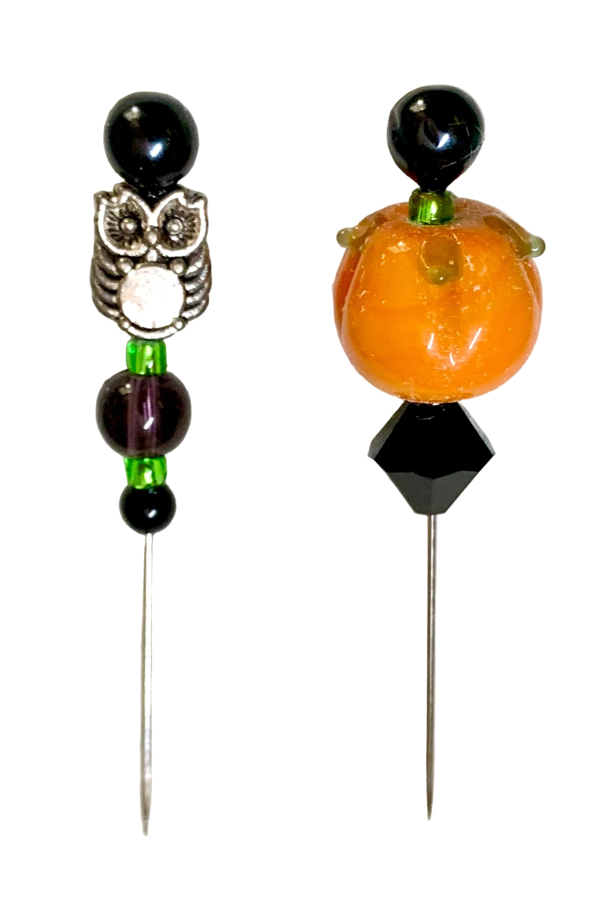 Two beaded pins displayed on a white background. The left pin features a silver owl charm with black, green, and purple beads. The right is a pumpkin.
[additional_image_link]