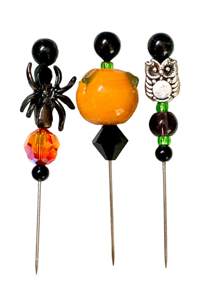 Three Halloween-themed beaded pins on metal needles, featuring a black spider, an orange pumpkin, and a silver owl design, displayed on a white background.
[additional_image_link]