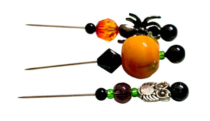 Three Halloween-themed beaded pins, featuring orange  fire bead,  green and black beads, a spider, a pumpkin, and a silver owl.
[additional_image_link]
